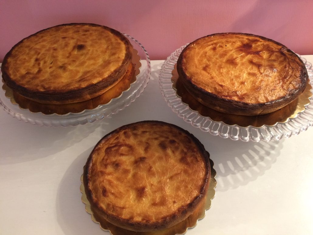 Tre pastiere di ricotta appena sfornate su alzate di vetro, contro la parete rosa del negozio
