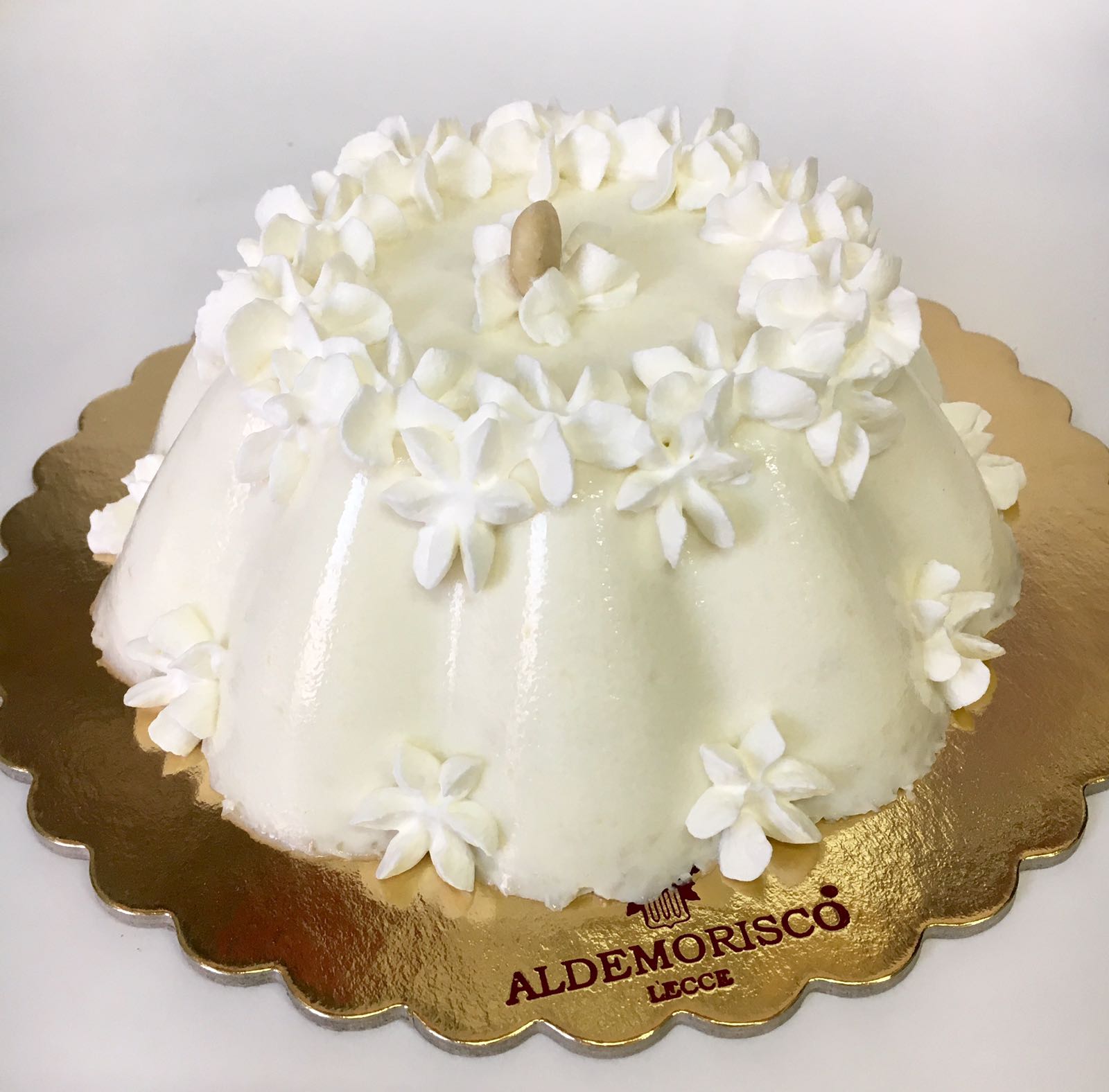 Spumone bianco decorato con fiori di panna, servito sul vassoio dorato con il marchio Aldemorisco Lecce
