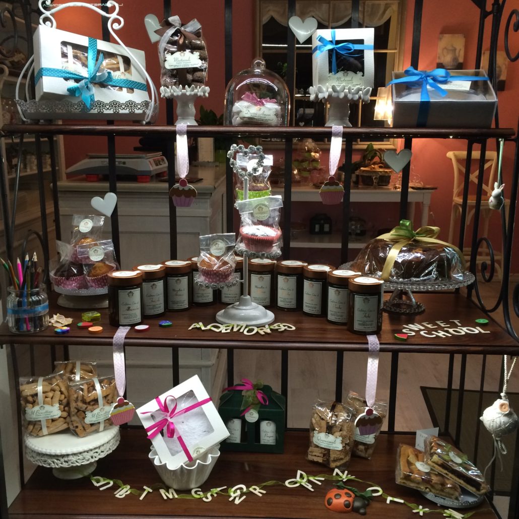 La vetrina di Aldemorisco vista dalla strada: biscotti confezionati, mustazzoli, vasetti di confettura e scatole regalo su una scaffalatura in ferro